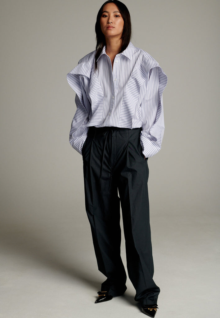 This cotton poplin shirt with a classic collar has six-hole buttons to adjust the neckline. Its cropped length accentuates the shirt's loose and open shape. Special detail with a panel of ruffles that creates a voluminous look to the garment.