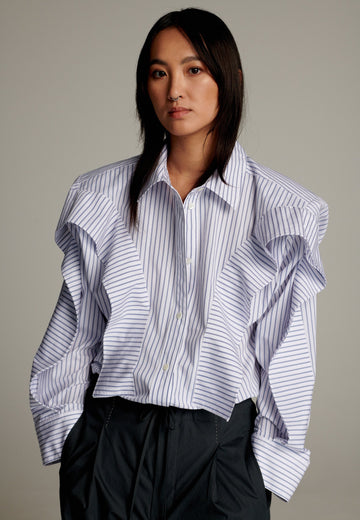 This cotton poplin shirt with a classic collar has six-hole buttons to adjust the neckline. Its cropped length accentuates the shirt's loose and open shape. Special detail with a panel of ruffles that creates a voluminous look to the garment.