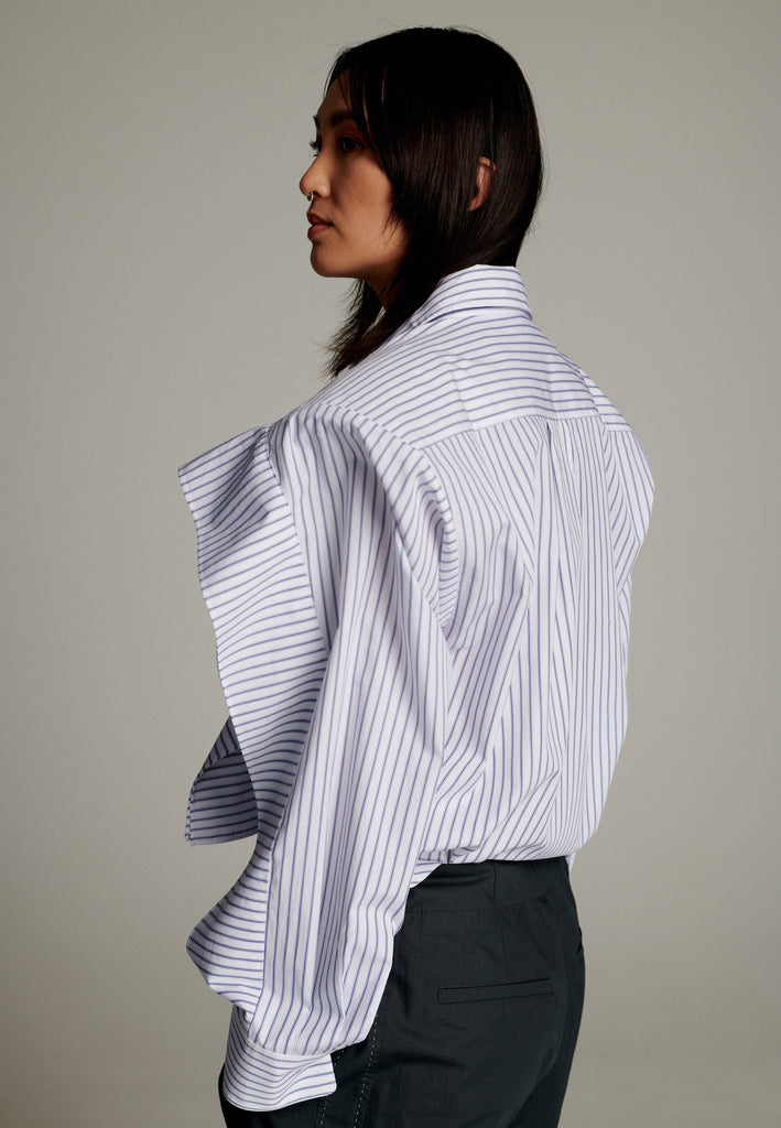 This cotton poplin shirt with a classic collar has six-hole buttons to adjust the neckline. Its cropped length accentuates the shirt's loose and open shape. Special detail with a panel of ruffles that creates a voluminous look to the garment.