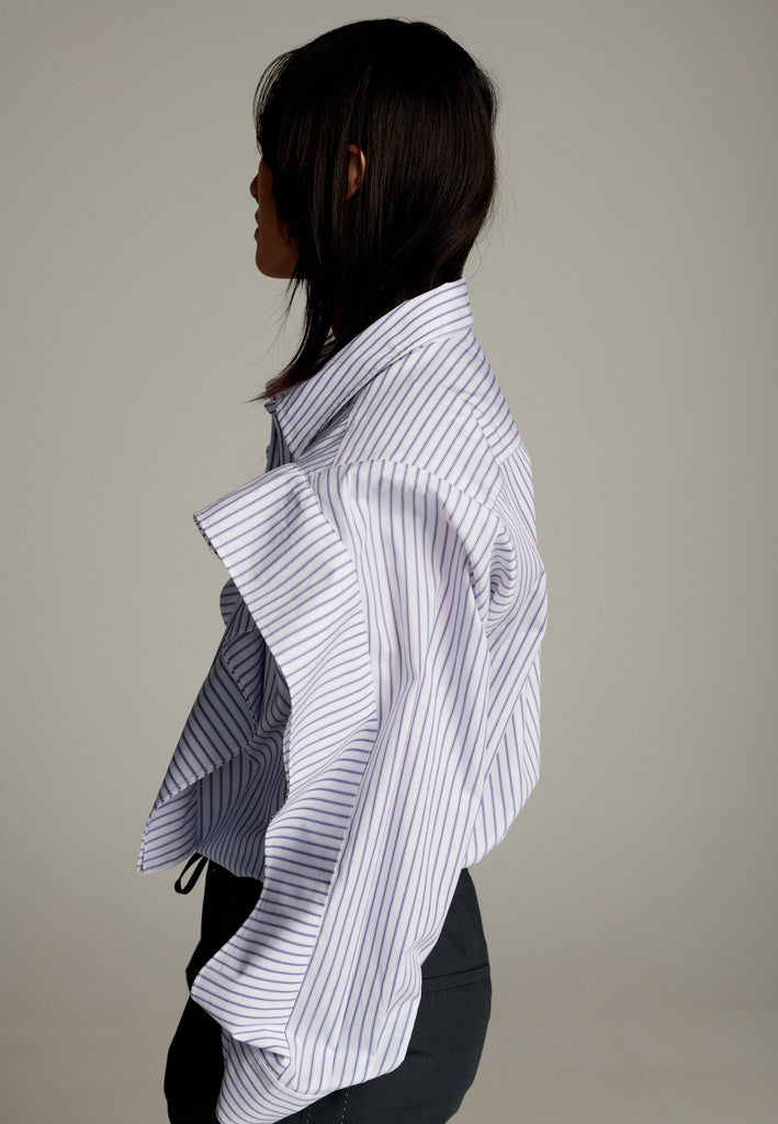 This cotton poplin shirt with a classic collar has six-hole buttons to adjust the neckline. Its cropped length accentuates the shirt's loose and open shape. Special detail with a panel of ruffles that creates a voluminous look to the garment.