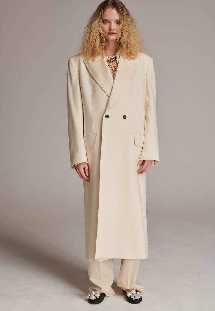 An effortless long coat to slip over any outfit. Detailed by sharp shoulder pads, double-breast fittin and square hole horn buttons. The ankle-grazing length emphasizes the loose fit and the effortless cool over tailoring. FRENKEN makes dressing up every morning easier.