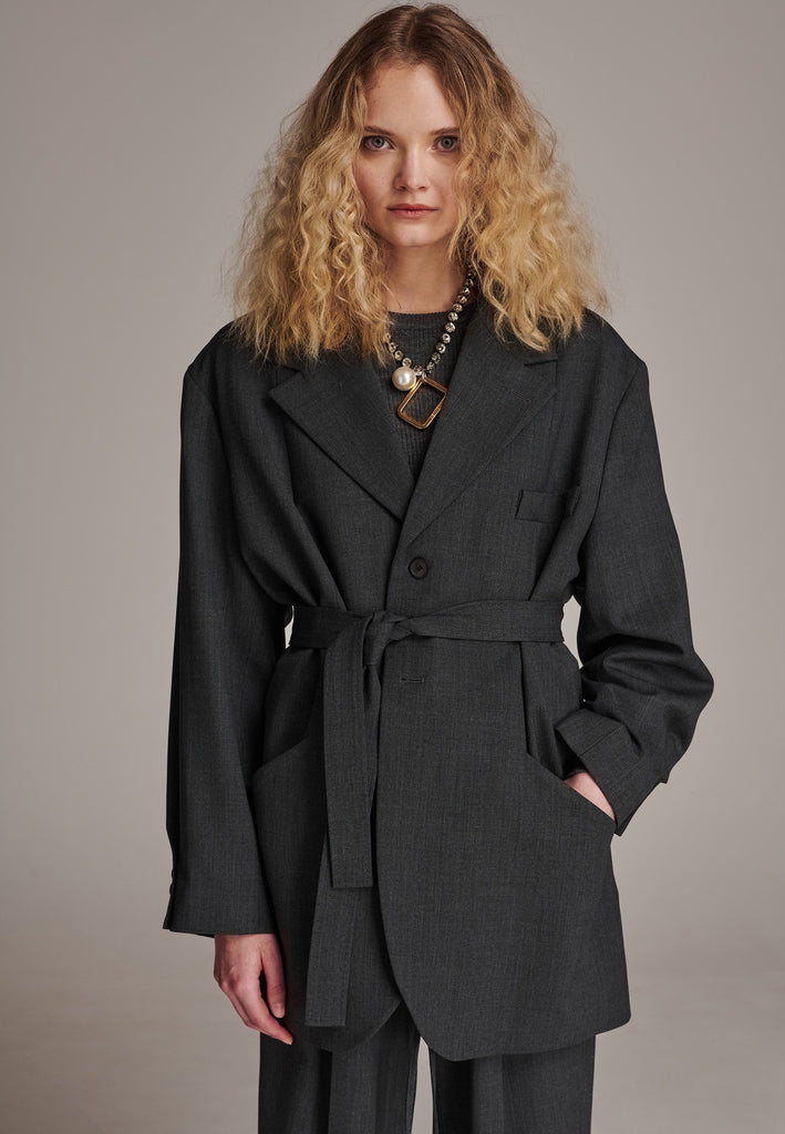 Oversized wrap blazer cut from a wool blend. Designed for an oversized fit, cut to be worn very loose. Padded wide round shoulders that add structure to the loose fit. Knot the inserted belt at the back or front to customize the shape. Horn button closure, welt pocket at front. Central vent at back hem. Full viscose satin lining and detailed with a needlepoint on the belt. This longline silhouette is perfectly tailored and could be your everyday rotation blazer.