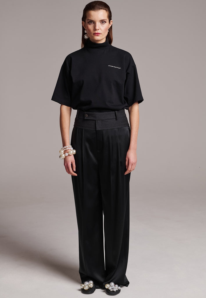 These deconstructed trousers combine a tailored wool top with a raw-edge finish, seamlessly attached to wide crepe satin legs that fall elegantly. The flat pleats create a slimmimg effect at the waist, enhancing the voluminous look of the wide legs. The pressed seam elongated the legs, ensuring a striking and sophisticated silhouette.