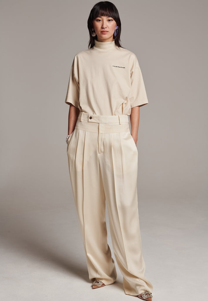 These deconstructed trousers combine a tailored wool top with a raw-edge finish, seamlessly attached to wide crepe satin legs that fall elegantly. The flat pleats create a slimmimg effect at the waist, enhancing the voluminous look of the wide legs. The pressed seam elongated the legs, ensuring a striking and sophisticated silhouette.