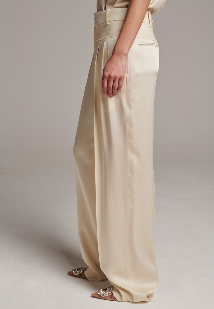 These deconstructed trousers combine a tailored wool top with a raw-edge finish, seamlessly attached to wide crepe satin legs that fall elegantly. The flat pleats create a slimmimg effect at the waist, enhancing the voluminous look of the wide legs. The pressed seam elongated the legs, ensuring a striking and sophisticated silhouette.