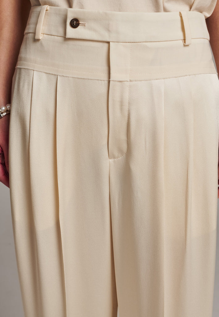 These deconstructed trousers combine a tailored wool top with a raw-edge finish, seamlessly attached to wide crepe satin legs that fall elegantly. The flat pleats create a slimmimg effect at the waist, enhancing the voluminous look of the wide legs. The pressed seam elongated the legs, ensuring a striking and sophisticated silhouette.