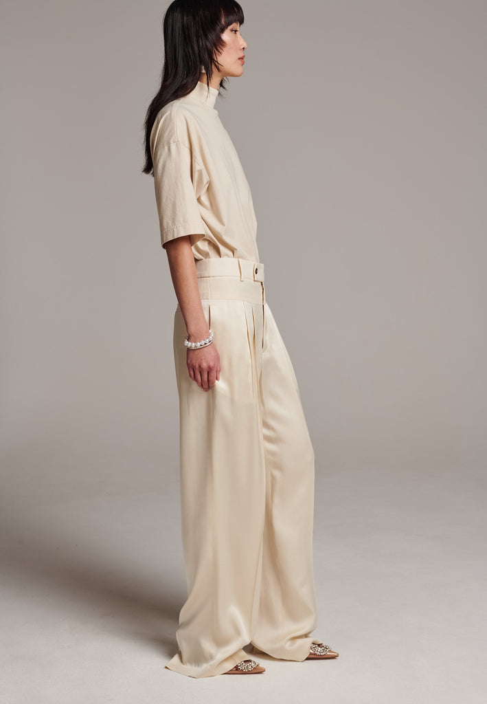 These deconstructed trousers combine a tailored wool top with a raw-edge finish, seamlessly attached to wide crepe satin legs that fall elegantly. The flat pleats create a slimmimg effect at the waist, enhancing the voluminous look of the wide legs. The pressed seam elongated the legs, ensuring a striking and sophisticated silhouette.