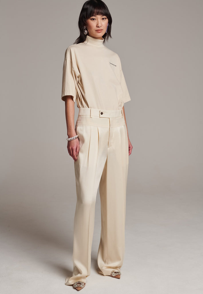 These deconstructed trousers combine a tailored wool top with a raw-edge finish, seamlessly attached to wide crepe satin legs that fall elegantly. The flat pleats create a slimmimg effect at the waist, enhancing the voluminous look of the wide legs. The pressed seam elongated the legs, ensuring a striking and sophisticated silhouette.