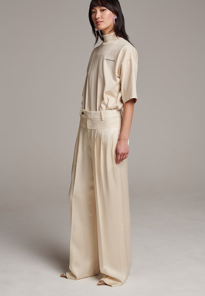 These deconstructed trousers combine a tailored wool top with a raw-edge finish, seamlessly attached to wide crepe satin legs that fall elegantly. The flat pleats create a slimmimg effect at the waist, enhancing the voluminous look of the wide legs. The pressed seam elongated the legs, ensuring a striking and sophisticated silhouette.