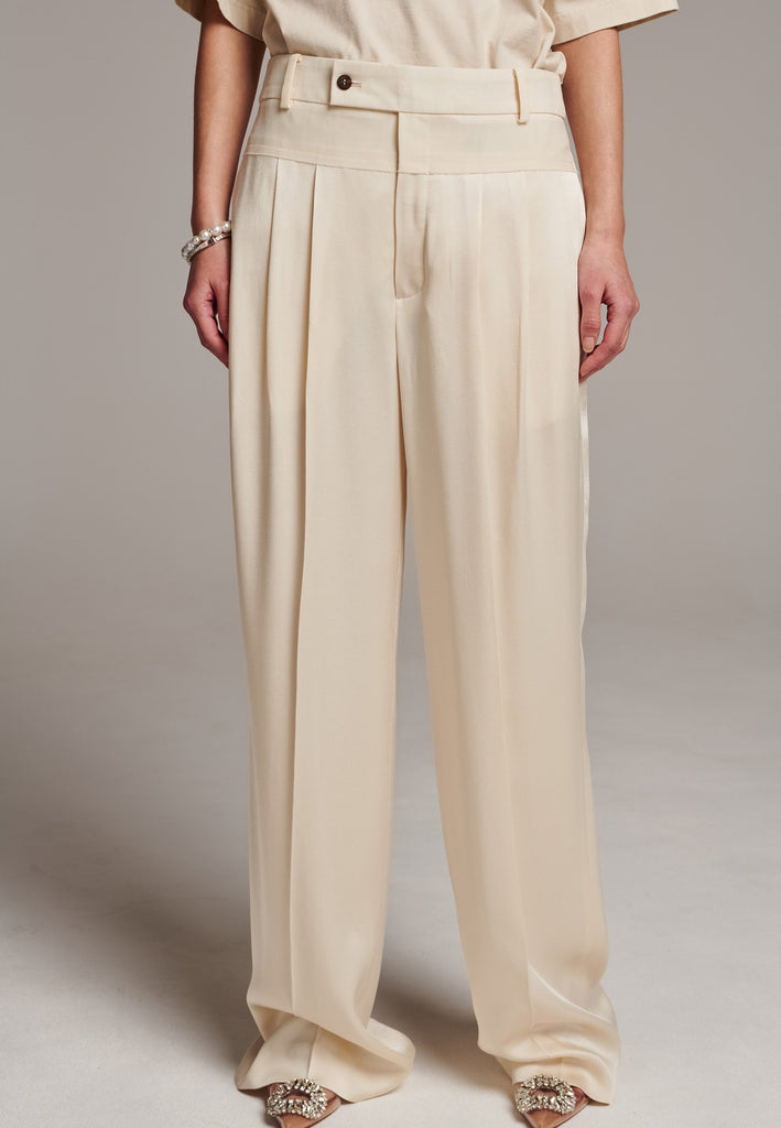 These deconstructed trousers combine a tailored wool top with a raw-edge finish, seamlessly attached to wide crepe satin legs that fall elegantly. The flat pleats create a slimmimg effect at the waist, enhancing the voluminous look of the wide legs. The pressed seam elongated the legs, ensuring a striking and sophisticated silhouette.