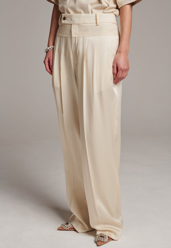 These deconstructed trousers combine a tailored wool top with a raw-edge finish, seamlessly attached to wide crepe satin legs that fall elegantly. The flat pleats create a slimmimg effect at the waist, enhancing the voluminous look of the wide legs. The pressed seam elongated the legs, ensuring a striking and sophisticated silhouette.