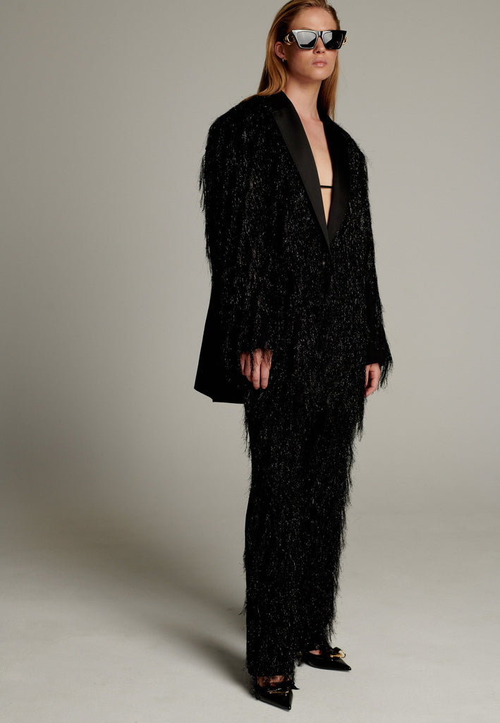 The pinnacle of sophistication with a bold touch. Crafted from elegant black fabric, it features an oversize cut that creates volume. Tinsel details add a modern and daring touch, perfect for glamorous evenings.