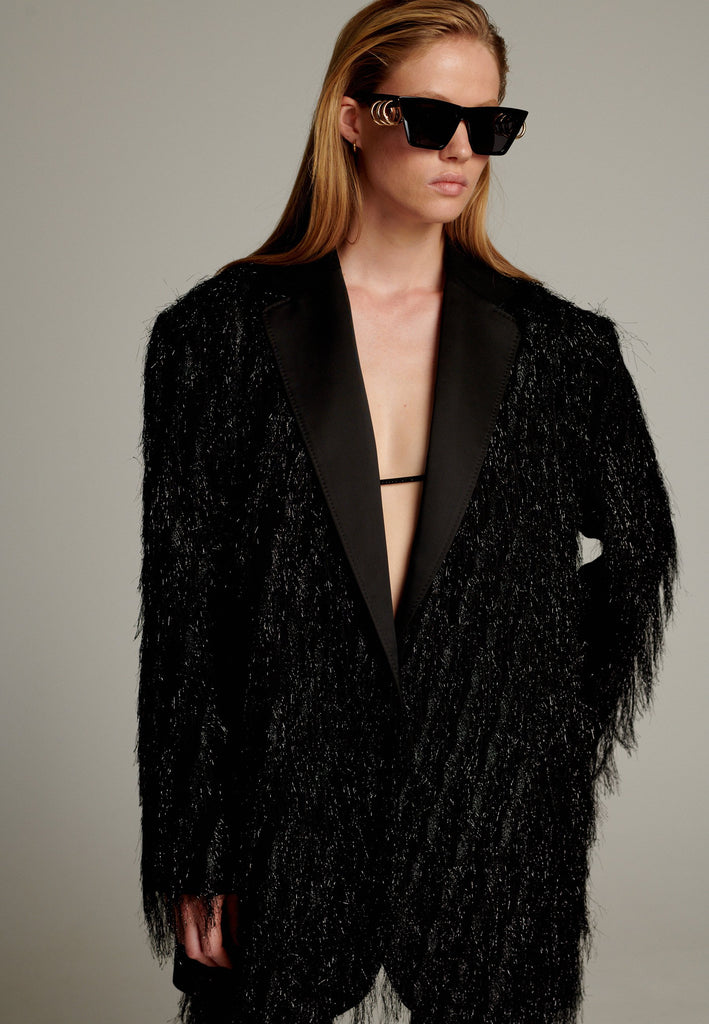 The pinnacle of sophistication with a bold touch. Crafted from elegant black fabric, it features an oversize cut that creates volume. Tinsel details add a modern and daring touch, perfect for glamorous evenings.