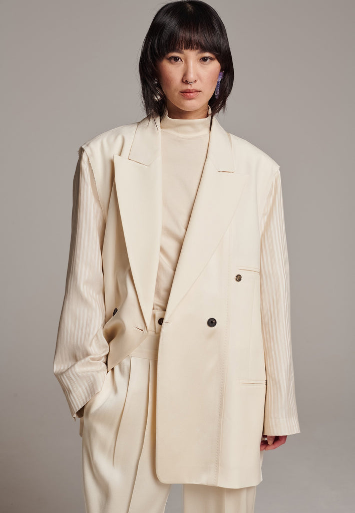 Perfectly tailored with a contemporary twist, this oversized blazer features unique inside-out details. The raw edge seam around the shoulder, where the tonal striped sleeve is set in, showcases its deconstructed design. Referencing the lining, the sleeve and welt pocket holds a charming Frenken lucky coin. A rounded insert at the back shoulder and refined darts enhance the sophisticated silhouette. Broad, soft shoulders, double-breasted horn buttons, and a fully satin-lined interior complete this standout 