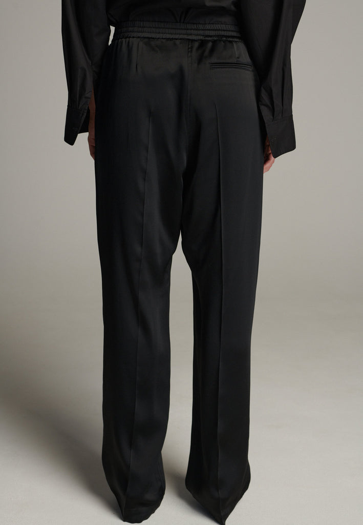 Crafted from smooth, high-quality crepe satin, they feature a relaxed, wide-leg silhouette inspired by traditional karate pants for a unique, contemporary twist. Designed with an elastic waistband, they offer a flexible, comfortable fit while maintaining a polished look. The elegant fabric drapes beautifully, creating fluid movement, making these trousers versatile enough to pair with both tailored blazers and casual tops.