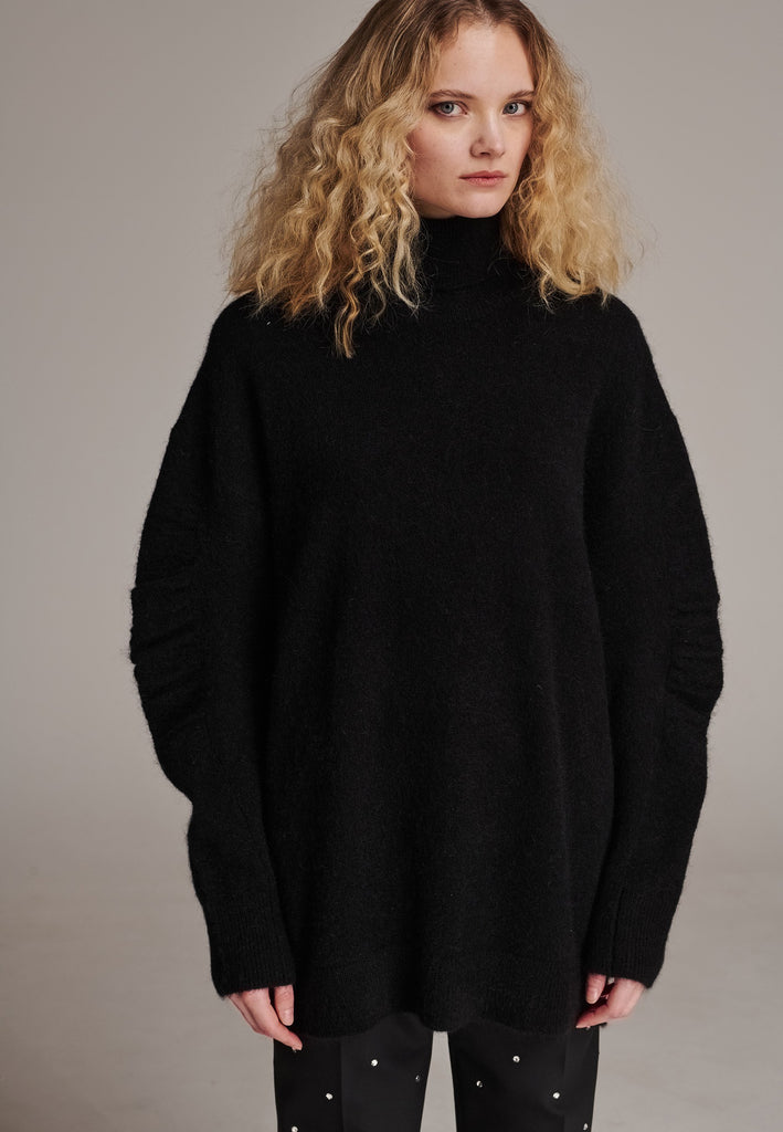 Stay warm and stylish with this oversized knitted sweater, crafted from luxurious virgin merino wool that gives a soft handle. Dropped shoulder seam detailed with gathering at the sleeves, it combines a cozy turtleneck with designer flair. The black shade works especially well with black tailoring and jeans. Designed for an oversized fit, cut to be worn very loose. Long in sleeves. This piece ensures you’ll stay snug and chic, even on the coldest days.