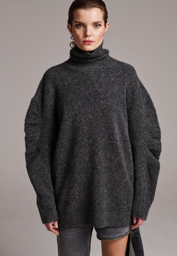 Stay warm and stylish with this oversized knitted sweater, crafted from luxurious virgin merino wool that gives a soft handle. Dropped shoulder seam detailed with gathering at the sleeves, it combines a cozy turtleneck with designer flair. This grey melange shade works especially well with black and grey tailoring and jeans. Designed for an oversized fit, cut to be worn very loose. Long in sleeves. This piece ensures you’ll stay snug and chic, even on the coldest days.