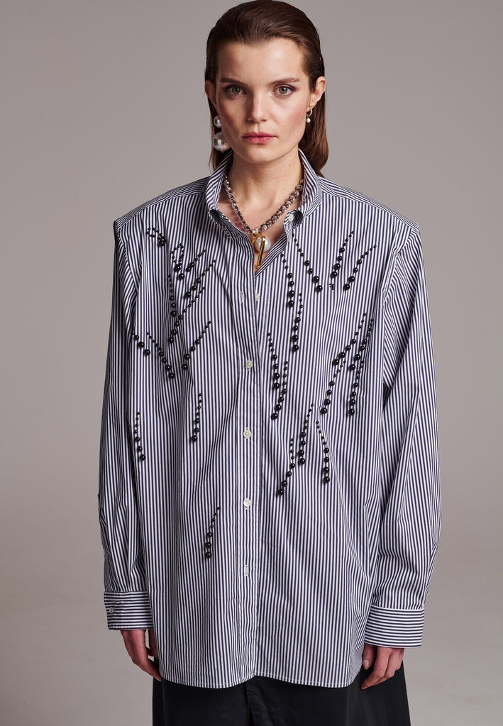 FRENKEN manages to create designs that are somehow classic yet totally modern at the same time. This oversized very easy-to-wear menswear shirt is a true homage to the eighties cut Ralph Lauren men's shirt. Dropped shoulders, with adjustable shoulder pads. Detailed with a mirrored F. Cut from 100% cotton poplin. This Ralf shirt is embellished with faux pearls in an increasing from small to large formation. It's an asset to your wardrobe.