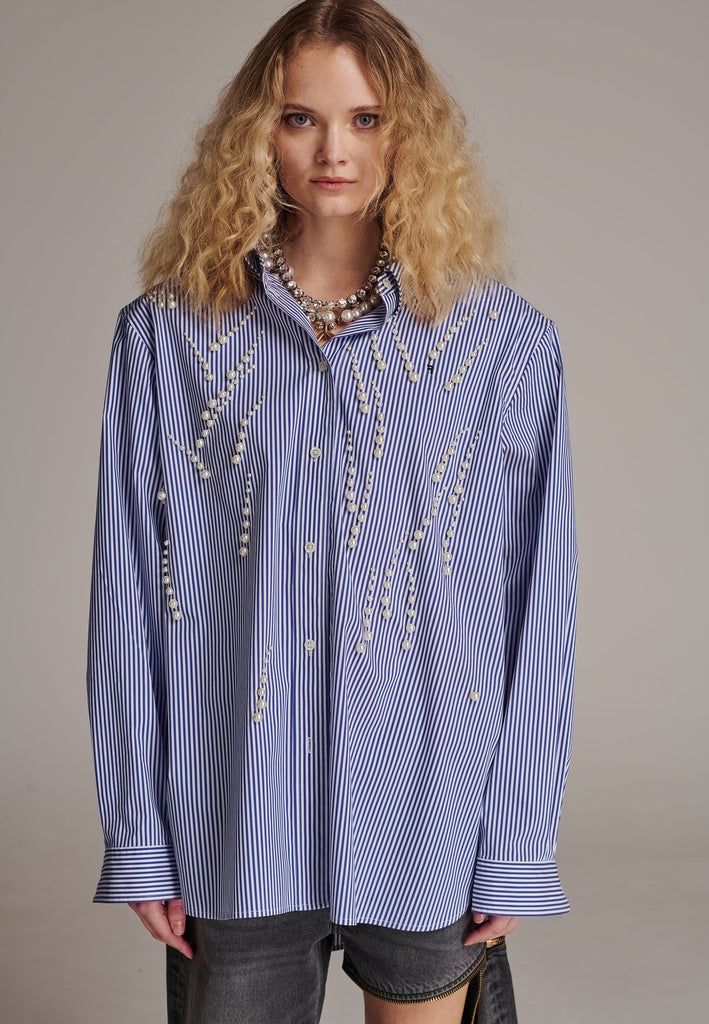 FRENKEN manages to create designs that are somehow classic yet totally modern at the same time. This oversized very easy-to-wear menswear shirt is a true homage to the eighties cut Ralph Lauren men's shirt. Dropped shoulders, with adjustable shoulder pads. Detailed with a mirrored F. Cut from 100% cotton poplin. This Ralf shirt is embellished with faux pearls in an increasing from small to large formation. It's an asset to your wardrobe.