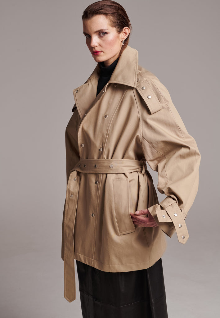 Introducing a short trench coat with a statement large collar and silver-tone snap buttons that are both visually appealing and functional. Adjustable snap buttons on the cuffs and belt ensure a customizable fit. Use the tie belt to cinch in at the waist. This versatile piece seamlessly blends style and practicality, making it a chic addition to any wardrobe. Intended for an oversized fit, cut to be worn very loose.