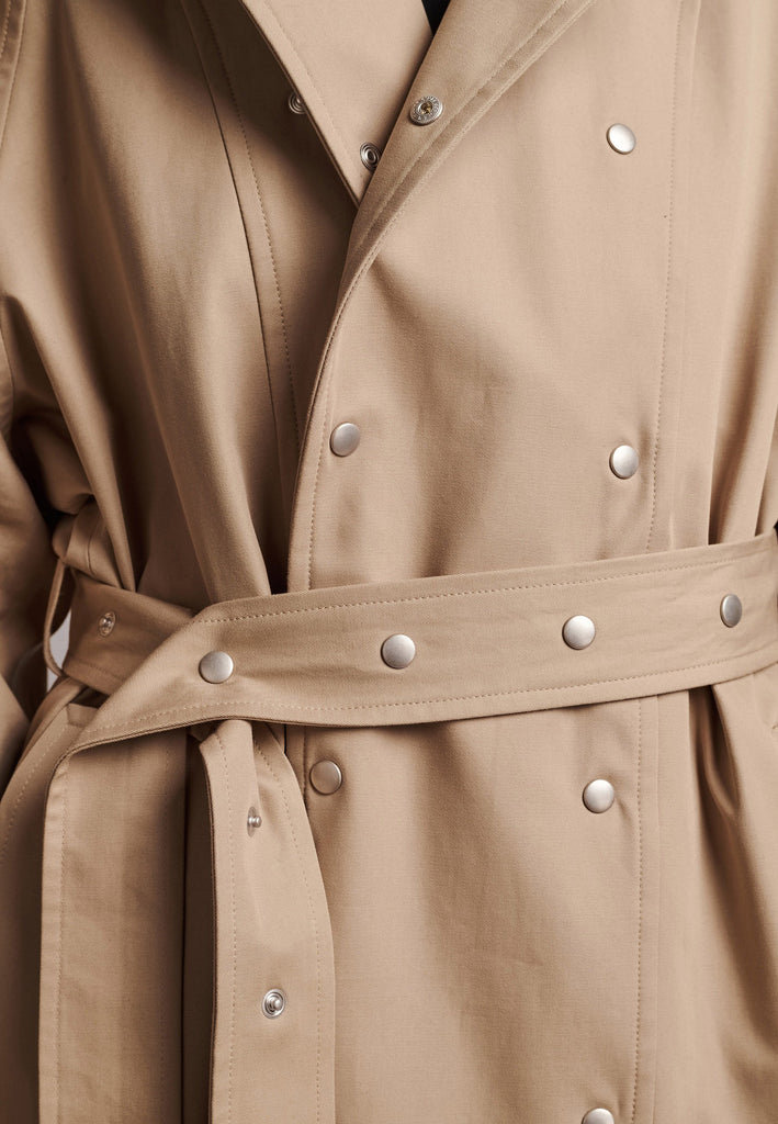 Introducing a short trench coat with a statement large collar and silver-tone snap buttons that are both visually appealing and functional. Adjustable snap buttons on the cuffs and belt ensure a customizable fit. Use the tie belt to cinch in at the waist. This versatile piece seamlessly blends style and practicality, making it a chic addition to any wardrobe. Intended for an oversized fit, cut to be worn very loose.