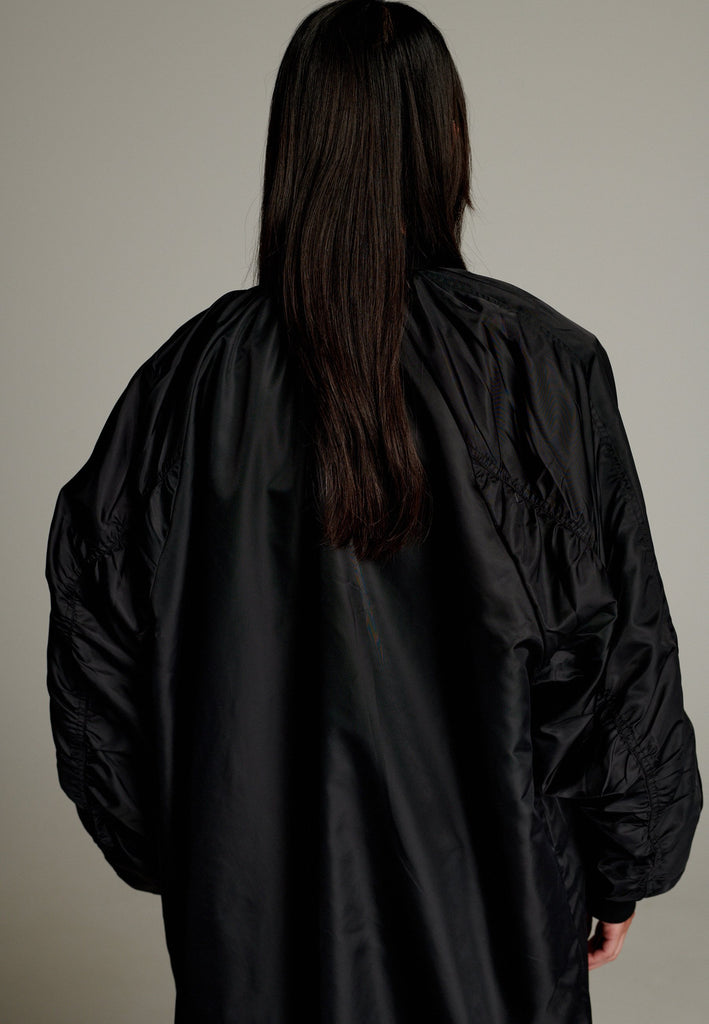 This long bomber jacket offers a perfect blend of modern style and functionality. It features two distinctive zipper closures—one in silver and the other in gold—on the sleeve, adding a bold, metallic contrast and unique detail. The elongated silhouette provides a sleek, urban look, while the durable nylon material ensures warmth and comfort.