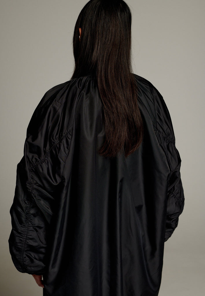 This long bomber jacket offers a perfect blend of modern style and functionality. It features two distinctive zipper closures—one in silver and the other in gold—on the sleeve, adding a bold, metallic contrast and unique detail. The elongated silhouette provides a sleek, urban look, while the durable nylon material ensures warmth and comfort.