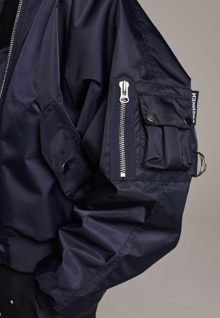 Our short bomber jacket maintains its oversized fit, crafted from crisp nylon in a deep navy blue. Adorned with silver hardware and zippers, this jacket adds a touch of edge to any outfit. Whether styled with tailored pants or a long skirt, it effortlessly enhances your look with a cool, contemporary flair.