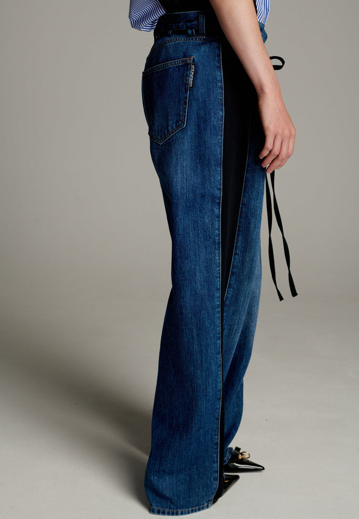 Where classic style meets with modern details. They offer the comfort and durability of traditional denim. A striking black panel along the lateral seams adds bold contrast, elevating their casual appeal. Featuring a black drawstring for an adjustable fit, these trousers combine functionality with a contemporary edge, making them perfect for versatile, everyday wear.