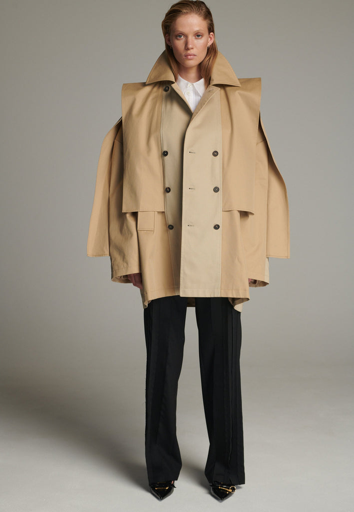 Inspired by a men's coat, FRENKEN offers a refined, contemporary twist on classic outerwear. Designed with dual-tone camel panels that create a subtle yet striking contrast, it exudes effortless sophistication. Featuring squared draped fabric, the coat showcases a modern, architectural design. Made from water-resistant cotton, it combines style, versatility, and functionality for everyday wear.