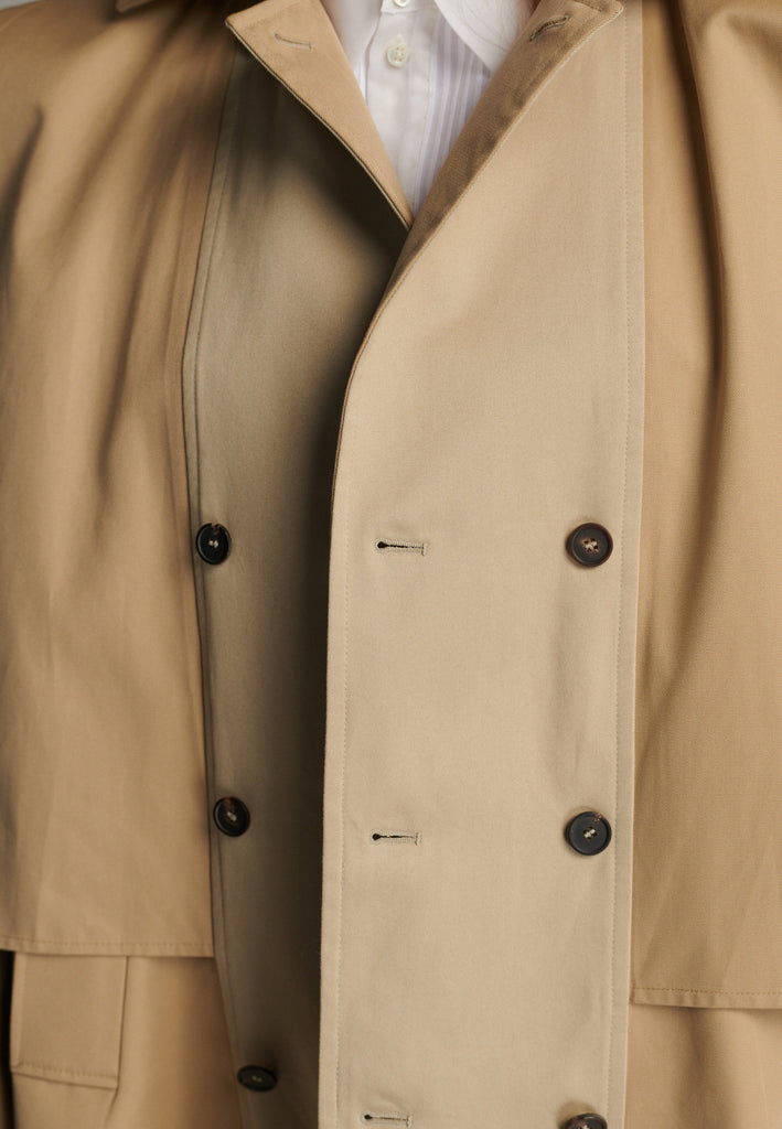 Inspired by a men's coat, FRENKEN offers a refined, contemporary twist on classic outerwear. Designed with dual-tone camel panels that create a subtle yet striking contrast, it exudes effortless sophistication. Featuring squared draped fabric, the coat showcases a modern, architectural design. Made from water-resistant cotton, it combines style, versatility, and functionality for everyday wear.