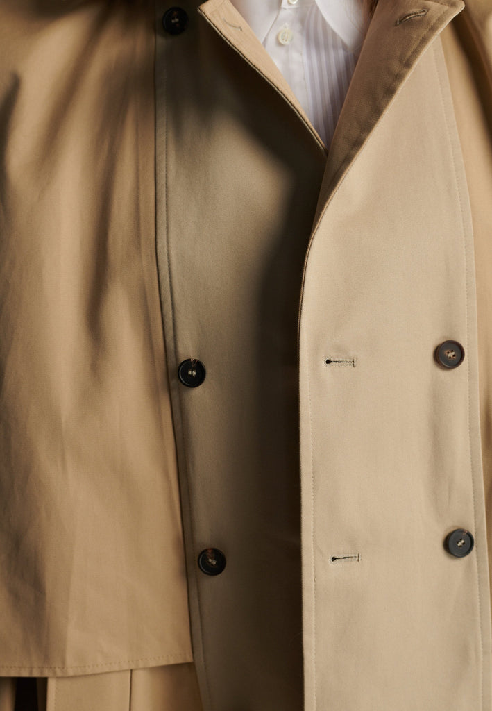 Inspired by a men's coat, FRENKEN offers a refined, contemporary twist on classic outerwear. Designed with dual-tone camel panels that create a subtle yet striking contrast, it exudes effortless sophistication. Featuring squared draped fabric, the coat showcases a modern, architectural design. Made from water-resistant cotton, it combines style, versatility, and functionality for everyday wear.