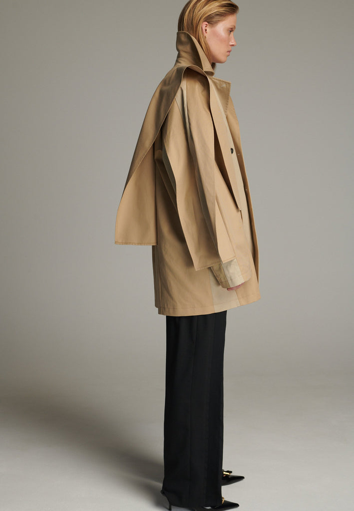 Inspired by a men's coat, FRENKEN offers a refined, contemporary twist on classic outerwear. Designed with dual-tone camel panels that create a subtle yet striking contrast, it exudes effortless sophistication. Featuring squared draped fabric, the coat showcases a modern, architectural design. Made from water-resistant cotton, it combines style, versatility, and functionality for everyday wear.