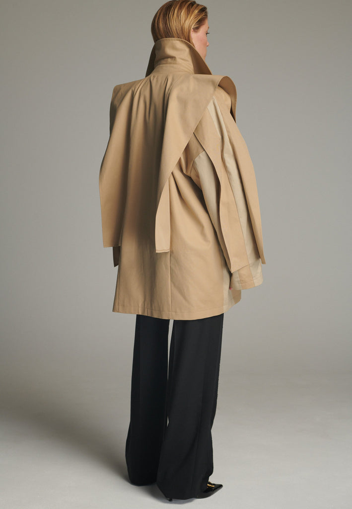 Inspired by a men's coat, FRENKEN offers a refined, contemporary twist on classic outerwear. Designed with dual-tone camel panels that create a subtle yet striking contrast, it exudes effortless sophistication. Featuring squared draped fabric, the coat showcases a modern, architectural design. Made from water-resistant cotton, it combines style, versatility, and functionality for everyday wear.