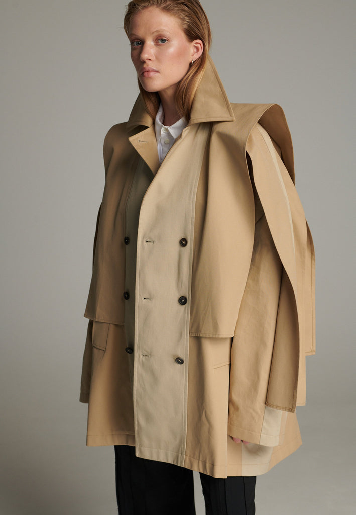 Inspired by a men's coat, FRENKEN offers a refined, contemporary twist on classic outerwear. Designed with dual-tone camel panels that create a subtle yet striking contrast, it exudes effortless sophistication. Featuring squared draped fabric, the coat showcases a modern, architectural design. Made from water-resistant cotton, it combines style, versatility, and functionality for everyday wear.