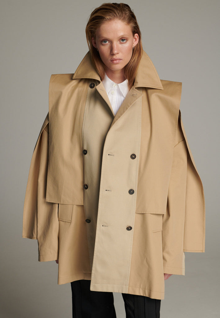 Inspired by a men's coat, FRENKEN offers a refined, contemporary twist on classic outerwear. Designed with dual-tone camel panels that create a subtle yet striking contrast, it exudes effortless sophistication. Featuring squared draped fabric, the coat showcases a modern, architectural design. Made from water-resistant cotton, it combines style, versatility, and functionality for everyday wear.