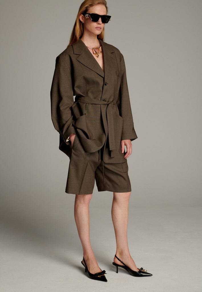 This elegant blazer is crafted in a luxurious camel melange wool, offering a soft and breathable feel perfect for summer wear. Its wrap-style design cinches at the waist, creating a flattering, tailored silhouette. Featuring contrasting stitching details, it adds a unique and stylish touch to the minimalist design. With clean lines and a sophisticated aesthetic, this blazer is a versatile addition to any wardrobe.