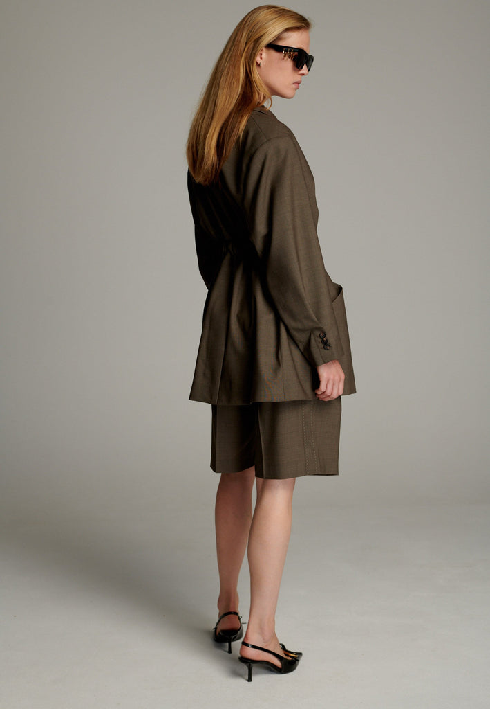 This elegant blazer is crafted in a luxurious camel melange wool, offering a soft and breathable feel perfect for summer wear. Its wrap-style design cinches at the waist, creating a flattering, tailored silhouette. Featuring contrasting stitching details, it adds a unique and stylish touch to the minimalist design. With clean lines and a sophisticated aesthetic, this blazer is a versatile addition to any wardrobe.