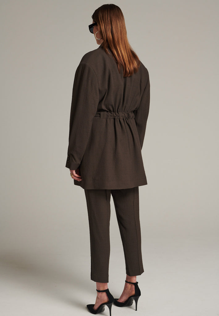 Seasonless oversized tailored blazer in choco with round-shouldered silhouette and coordinating belt that creates some gathering at the back to temper the fitting. Play with it and tie at the smallest part of your waist or tie it at the back for a sense of ease.