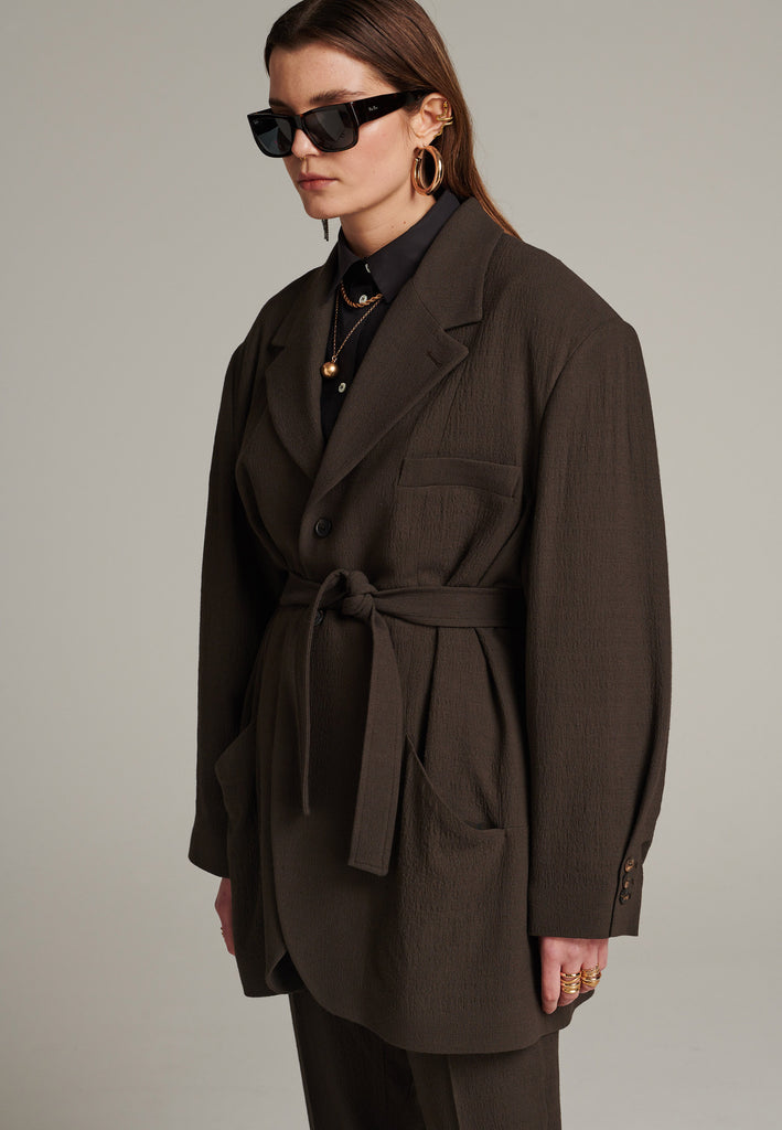 Seasonless oversized tailored blazer in choco with round-shouldered silhouette and coordinating belt that creates some gathering at the back to temper the fitting. Play with it and tie at the smallest part of your waist or tie it at the back for a sense of ease.