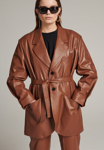 Seasonless oversized leather blazer in cognac with round-shouldered silhouette and coordinating belt that creates some gathering at the back to temper the fitting. Play with it and tie at the smallest part of your waist or tie it at the back for a sense of ease. Pockets, horn buttons and fully lined with. Double fun: wear it as a blazer or as a jacket.