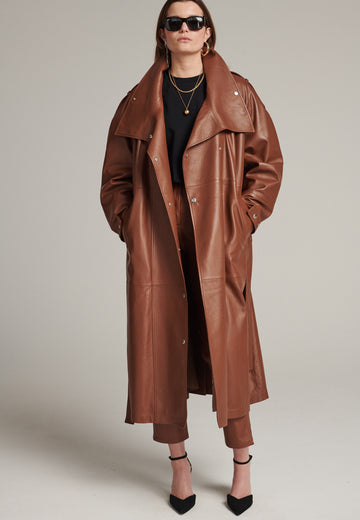 Oversized trench coat crafted in butterly soft lamb leather in cognac. Detailed with silver metal press buttons at front closure, epaulettes at shoulders and cuffs. Designed with a maxi collar with the snap-fastening buttons and a self-leather belt tp cinch the loose oversized fit.