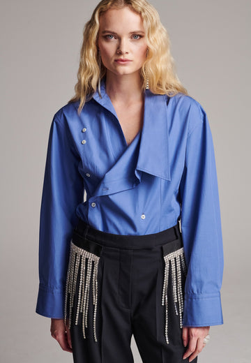 Wide-shouldered asymmetric wrap shirt fitted at the waist. Asymmetric collar structure. Wide relaxed sleeves with multiple buttons on the cuff to adjust the width. Detailed with darts at the waist and six-hole buttons. Cut from crispy cotton poplin.